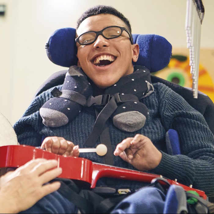 a teenaged boy smiling during his music therapy session with a demelza healthcare assistant and his parent