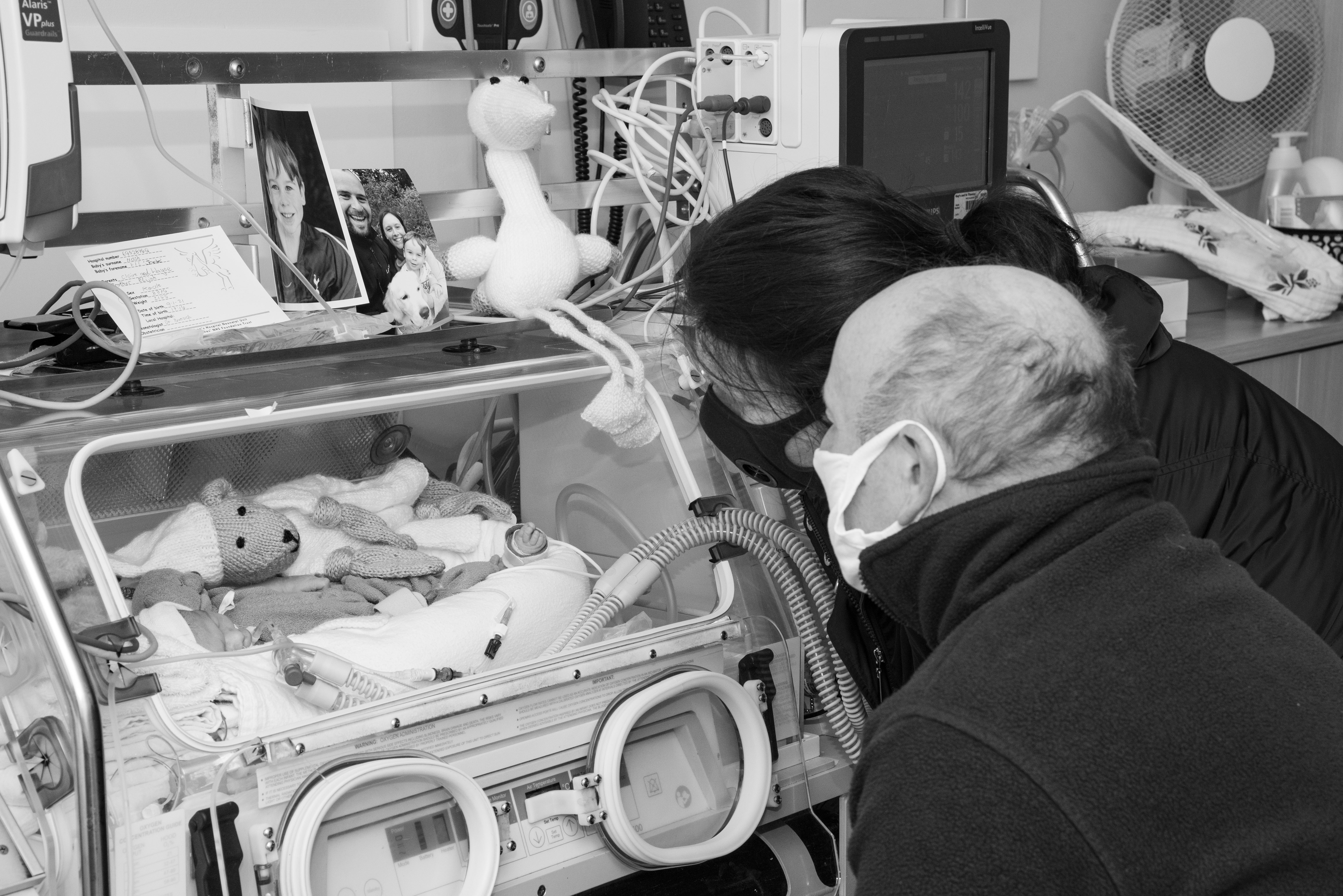 Two grandparents look in on their baby granddaughter, who is laying in an incubator.