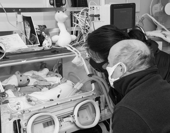 Two grandparents look in on their baby granddaughter, who is laying in an incubator.