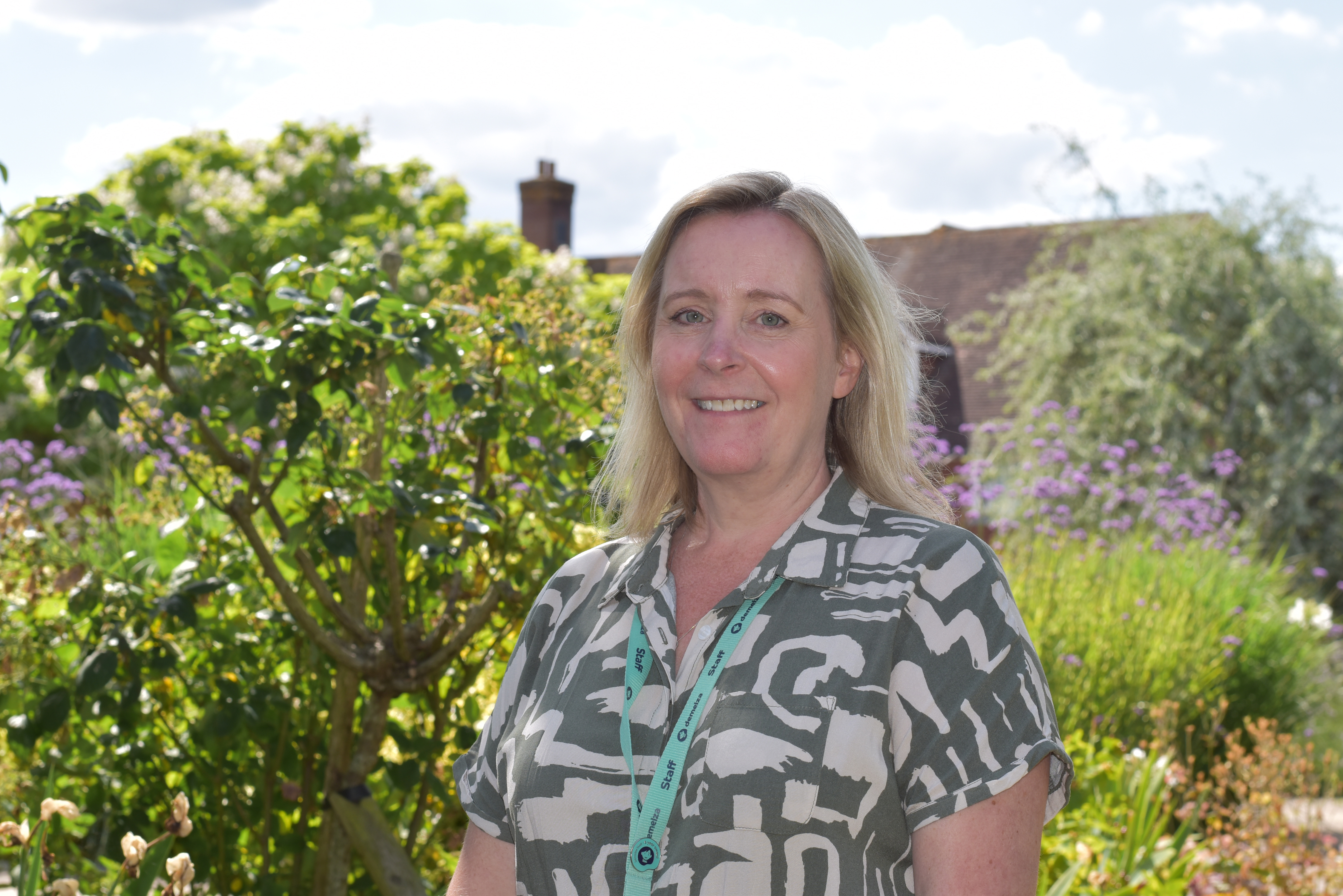 Katie Stevens, Director of Clinical Services, stands in Demelza’s gardens wearing a patterned top and smiling.