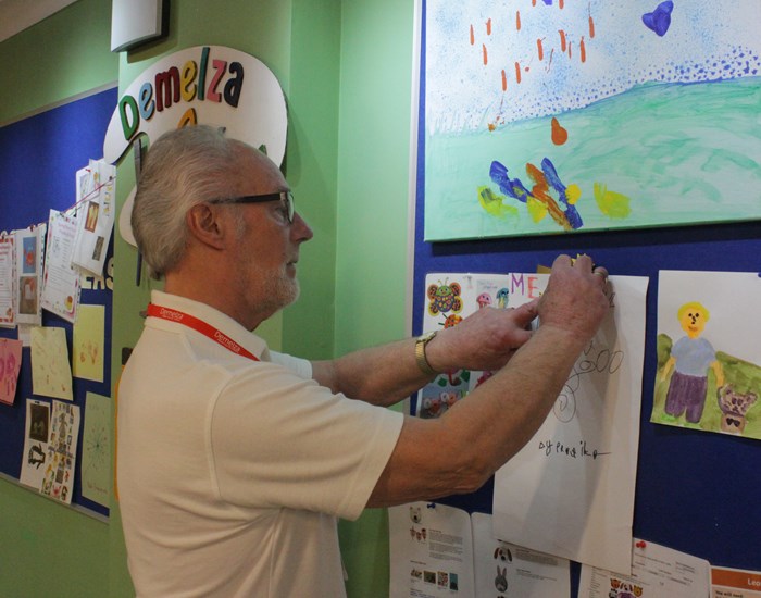 Volunteer, Dave, pinning art to an announcement board.