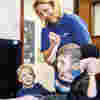 A Demelza nurse smiling while holding hands of a young child in a chair