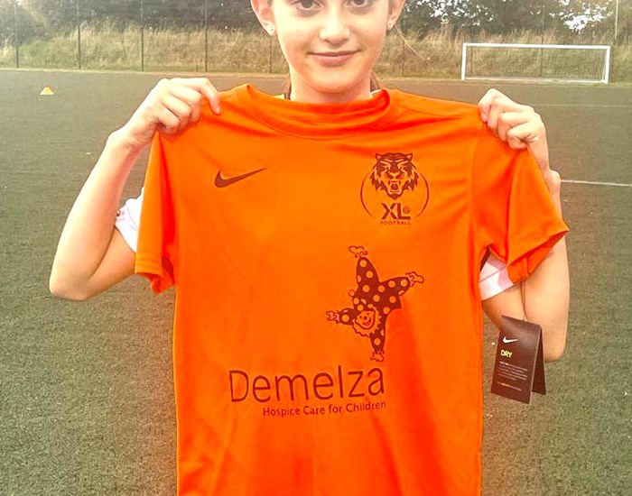 A female football player holds up her match day shirt, with the Demelza logo on it.