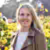 Trustee Heather Lucas smiles in sunny gardens, wearing a cream jumper and tan suede jacket.