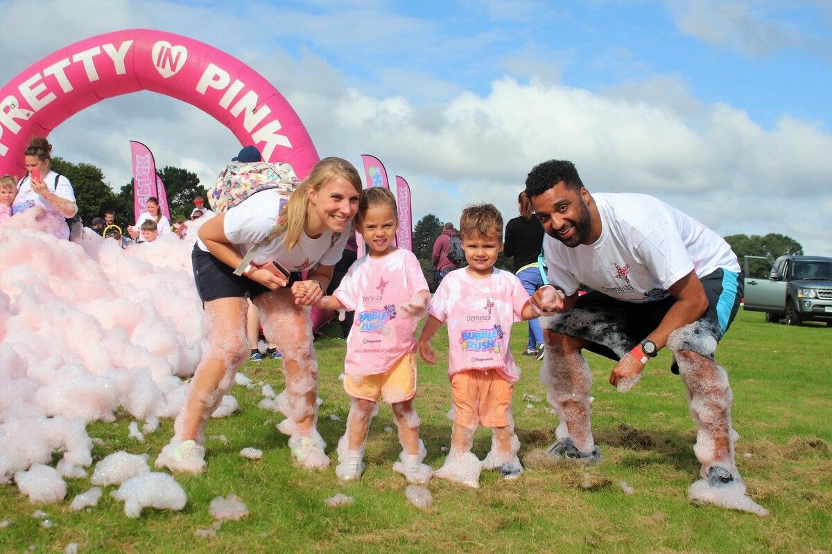 Family at Bubble Rush in Mote Park, Kent, smiling and covered in pink foam bubbles.