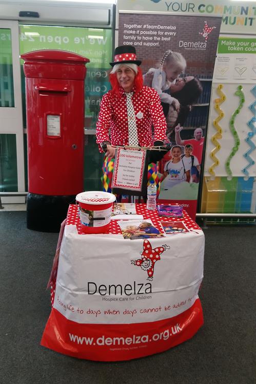 Tim is kitted out in Demelza red and white polka dots, standing behind a fundraising stand.