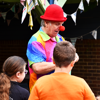 A man with a red nose, hat and a rainbow coloured shirt with two young boys and one young girl at Family Fun Day