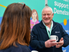 A man with white hair holding a mug smiling while talking to a woman with brown hair