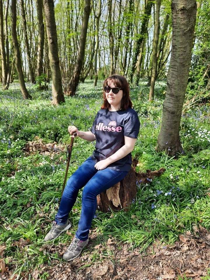 Volunteer Maggie sitting on tree stump in forest, wearing sunglasses