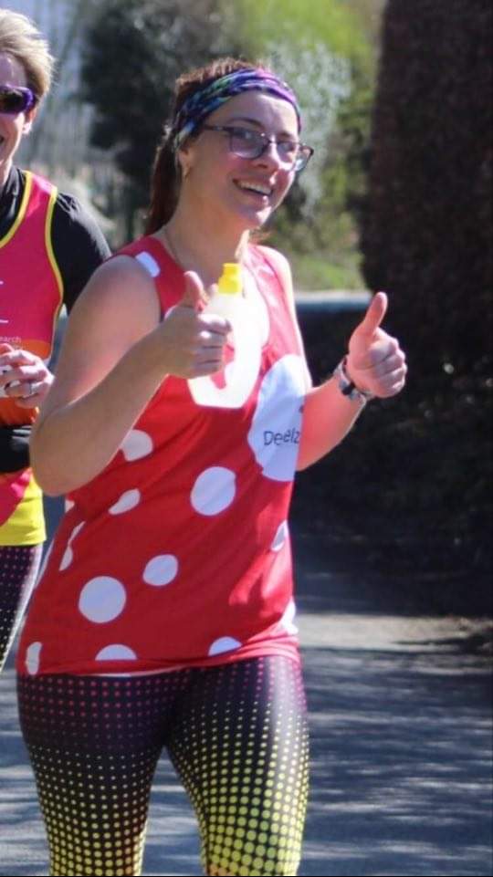 Lyn is running in her dotty Demelza vest, with her thumbs up.