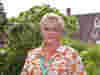 Demelza CEO Lavinia Jarrett stands in the hospice gardens, wearing a bright top and jewellery, smiling warmly.