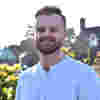 Trustee Rory Burns stands smiling in sunny gardens, wearing a pale blue shirt.
