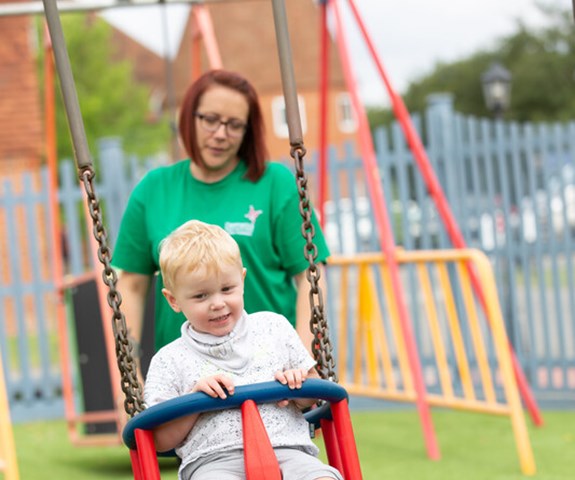Nursing Associate Becky, plays with Ralph on the swings in the playground at Demelza Kent.