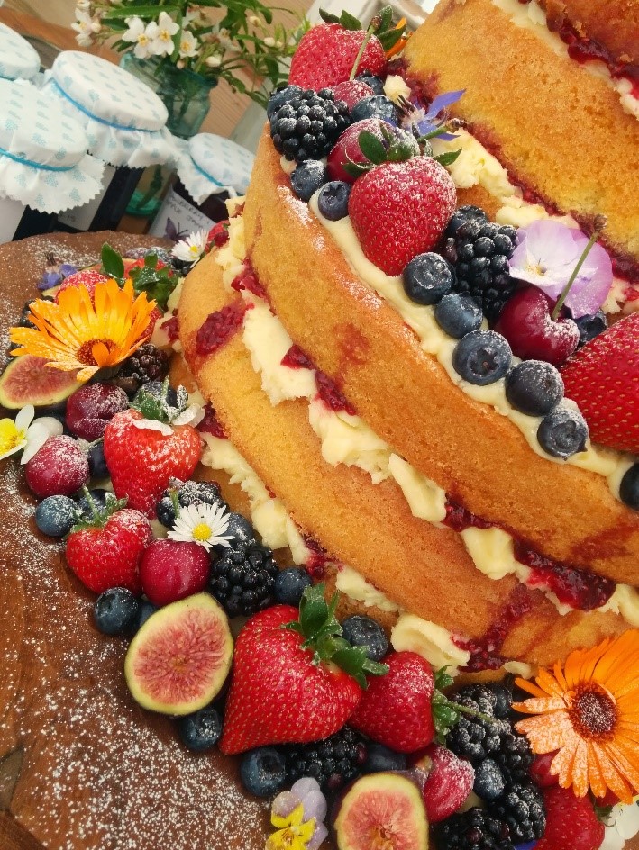 A large, multilayer Victoria sponge cake, beautifully decorated with a variety of fruit.