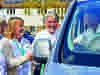 Four people wearing Demelza lanyards interacting near a Demelza vehicle; three stand outside while one is seated inside.
