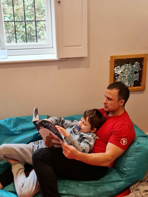 Oakley lays in his Dad. His dad is reading him a book.