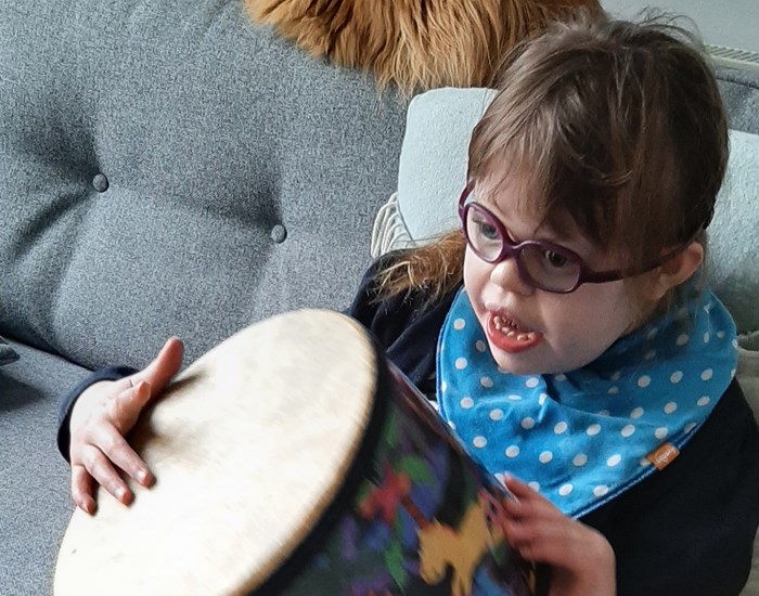 Lucy is sitting on her sofa, holding and playing her drum.
