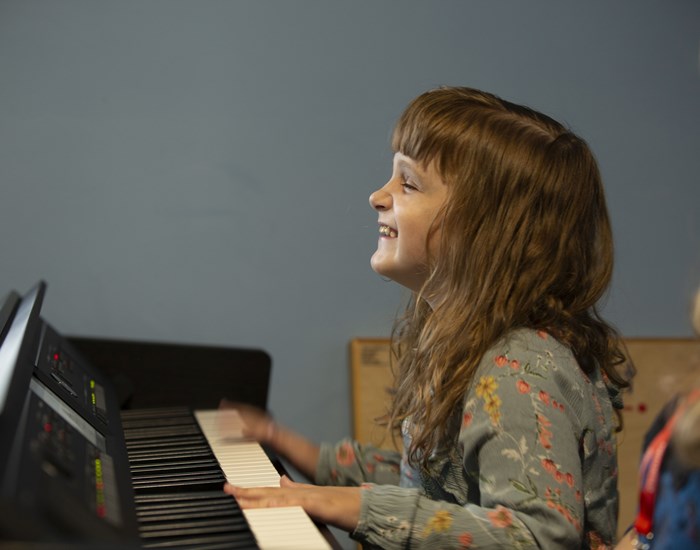 Hallie is laughing, whilst playing the piano in the music room.