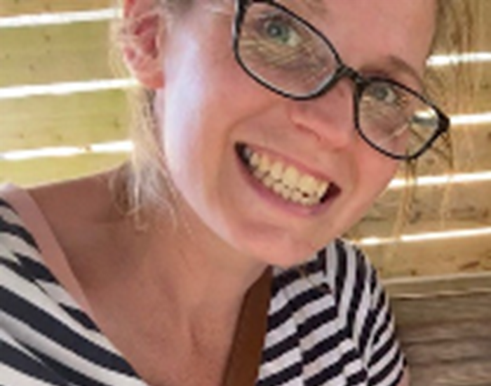 Hannah is smiling, wearing glasses and wearing a navy and white stripe t-shirt.