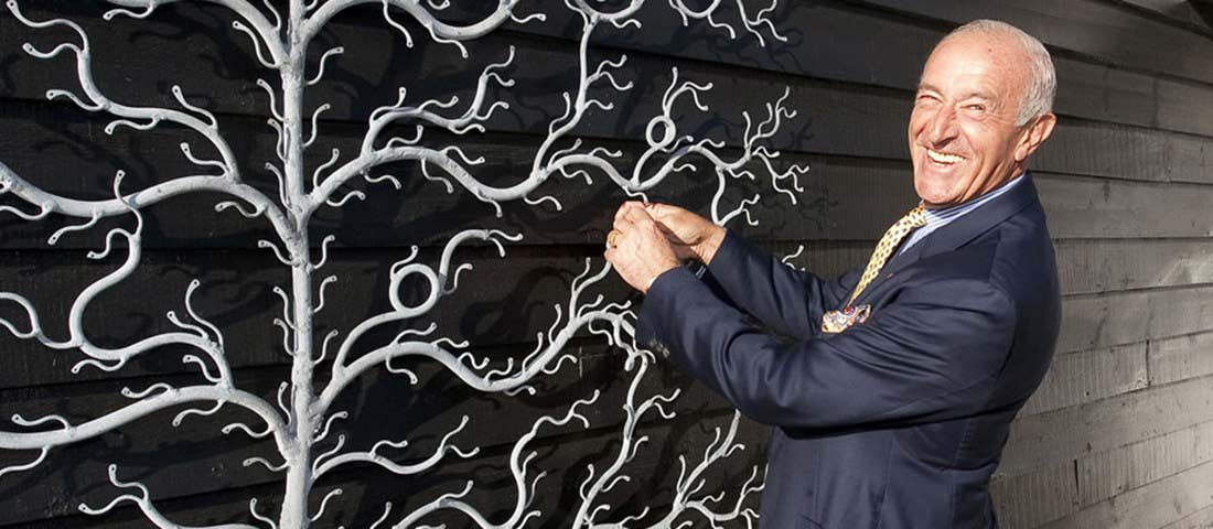 Len Goodman smiles broadly at the 2013 launch of the Goodman Celebration Tree, wearing a smart navy blue suit and tie.