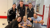 A child in a wheelchair surrounded by his parents and a few players from Fulham football club smiling towards the camera with a thumbsup