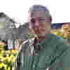 Sir Richard Douglas stands in sunny gardens, wearing a green khaki shirt.