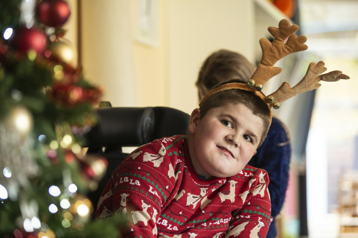 Curtis is wearing a Christmas jumper, reindeer antlers and looking at a brightly lit Christmas tree.