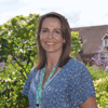 Deputy CEO Hayley Richardson stands smiling in the sunny gardens at Demelza, wearing a bright blue outfit.