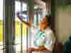 Volunteer in white uniform and lanyard, hair tied back, cleaning glass doors overlooking an outdoor area.