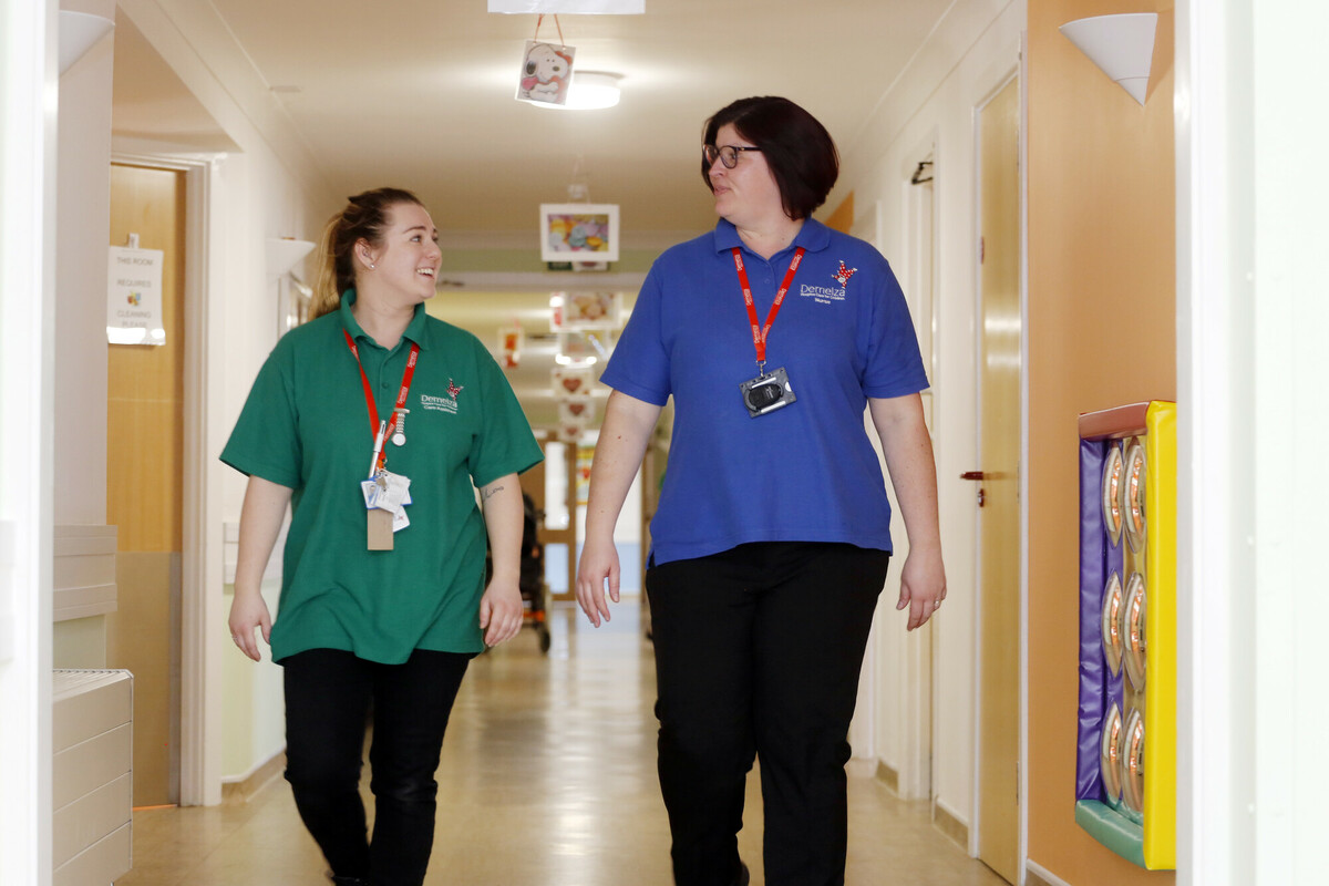 A registered nurse and health care assistant walk together along the care corridor at Demelza.