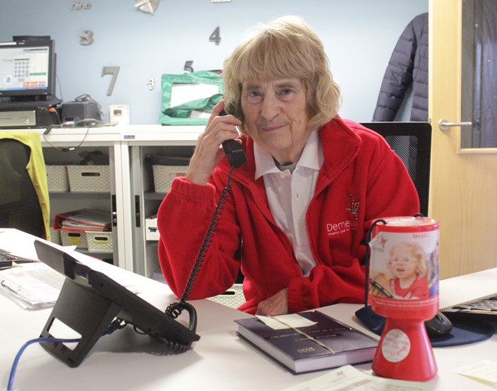 A receptionist wearing a red fleece is on the phone.