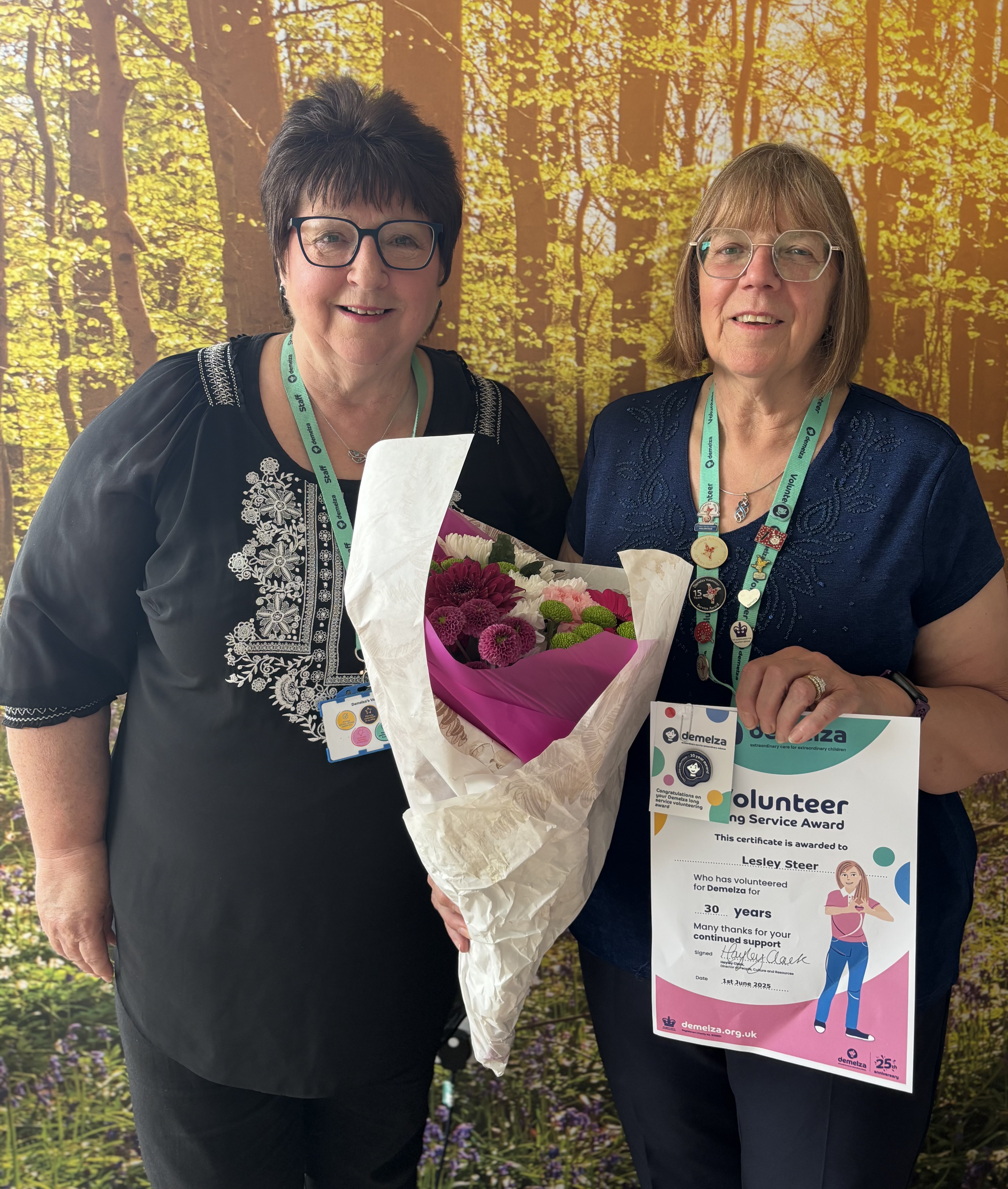 Fundraising volunteer Lesley smiles while receiving her 30 Years Long Service Award, holding a bright bouquet and certificate.