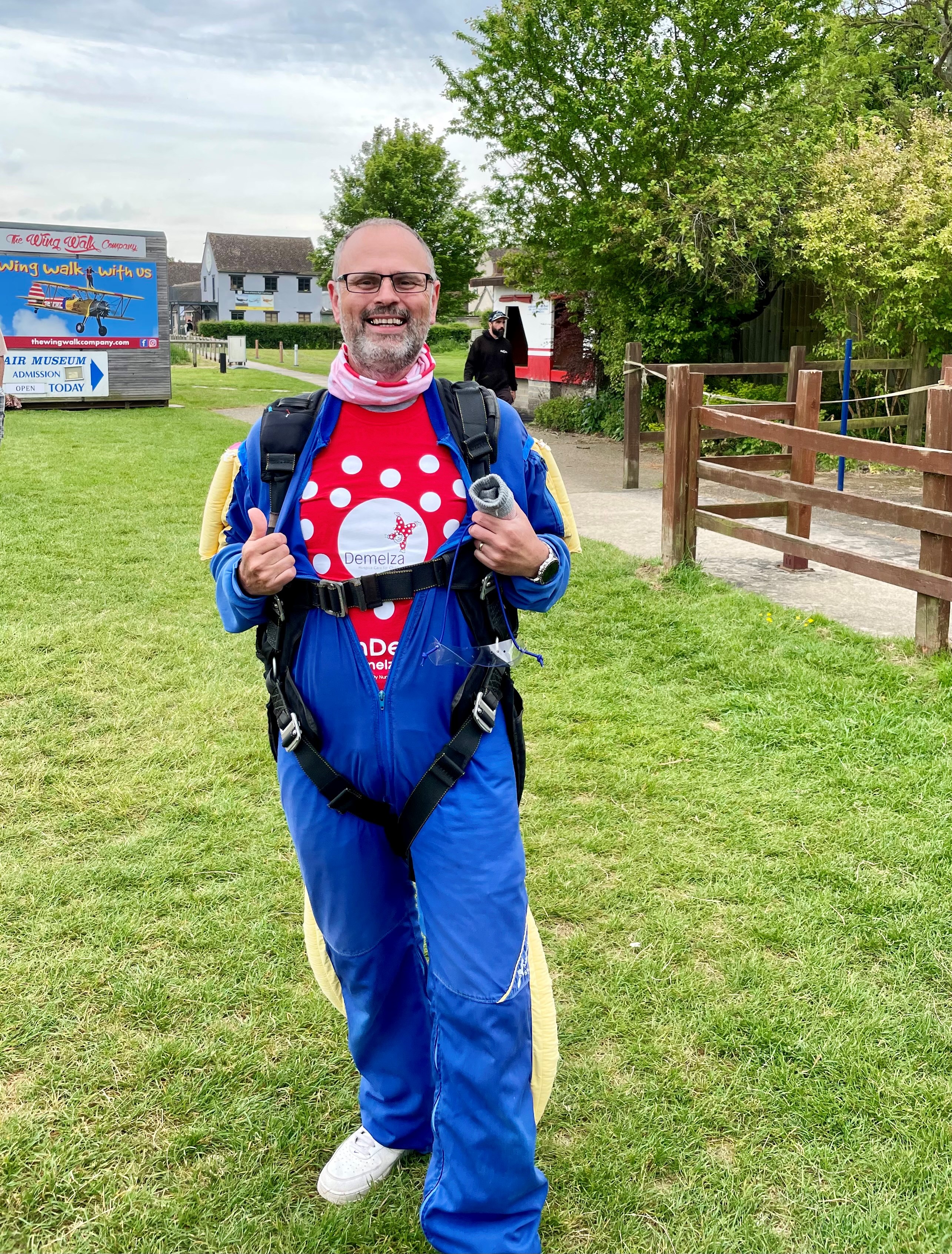 A charity skydiver is wearing his skydive jumpsuit, pulling open the chest to show his Demelza t-shirt underneath.