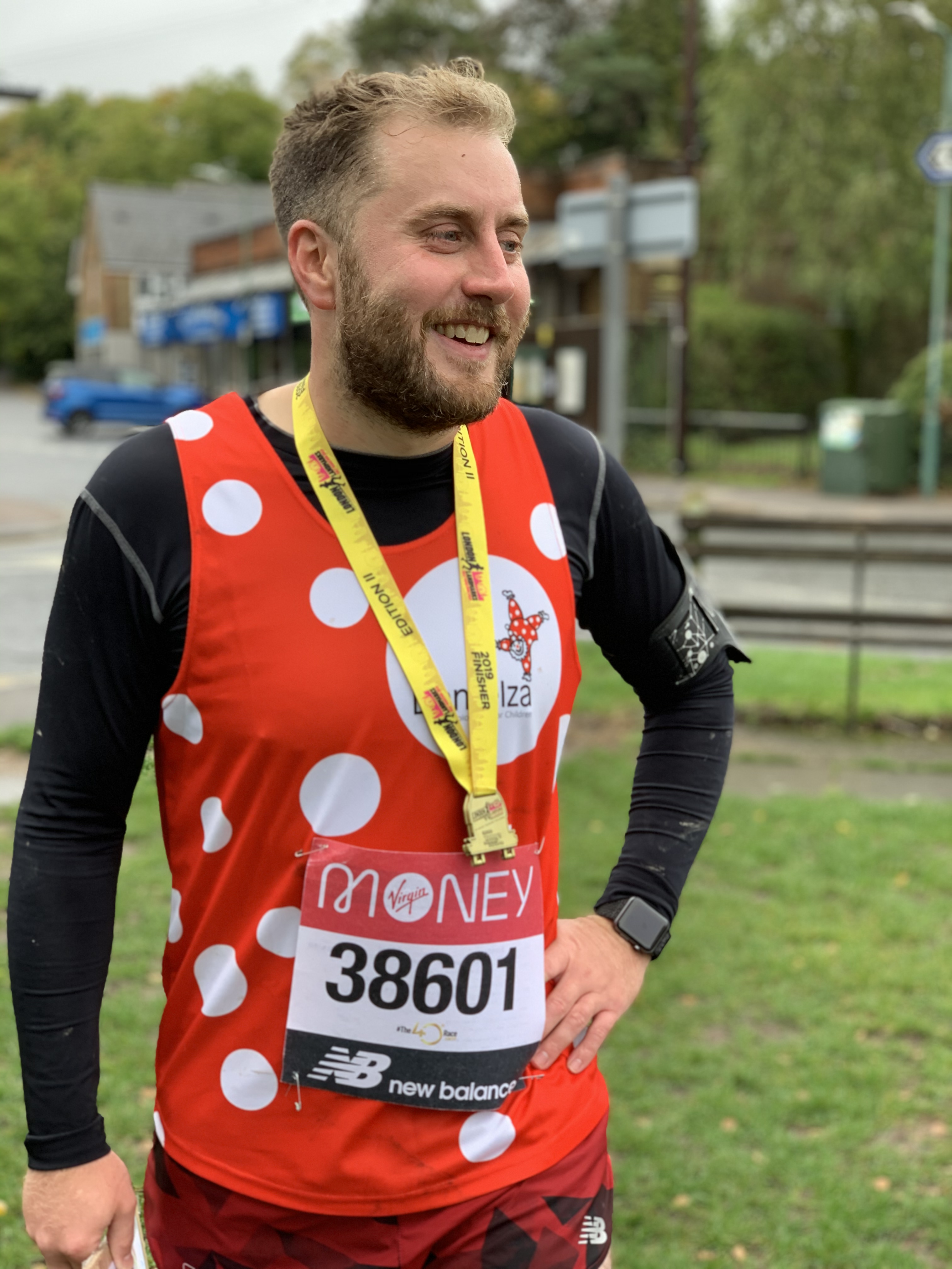 Gavin is wearing his Demelza dotty running vest over a black long sleeve top, wearing a medal.