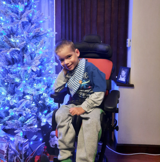 Finlay sits next to a blue, sparkling Christmas tree.