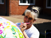Woman with sunglasses on head painting a colourful Demelza sculpture outdoors, with a brick building visible in the background.