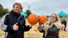 Male and female holding up pumpkins and smiling at Demelza Pumpkin Patch event