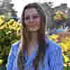 Associate Trustee Lucille Harvey stands smiling in sunny gardens, wearing a blue stripy shirt.