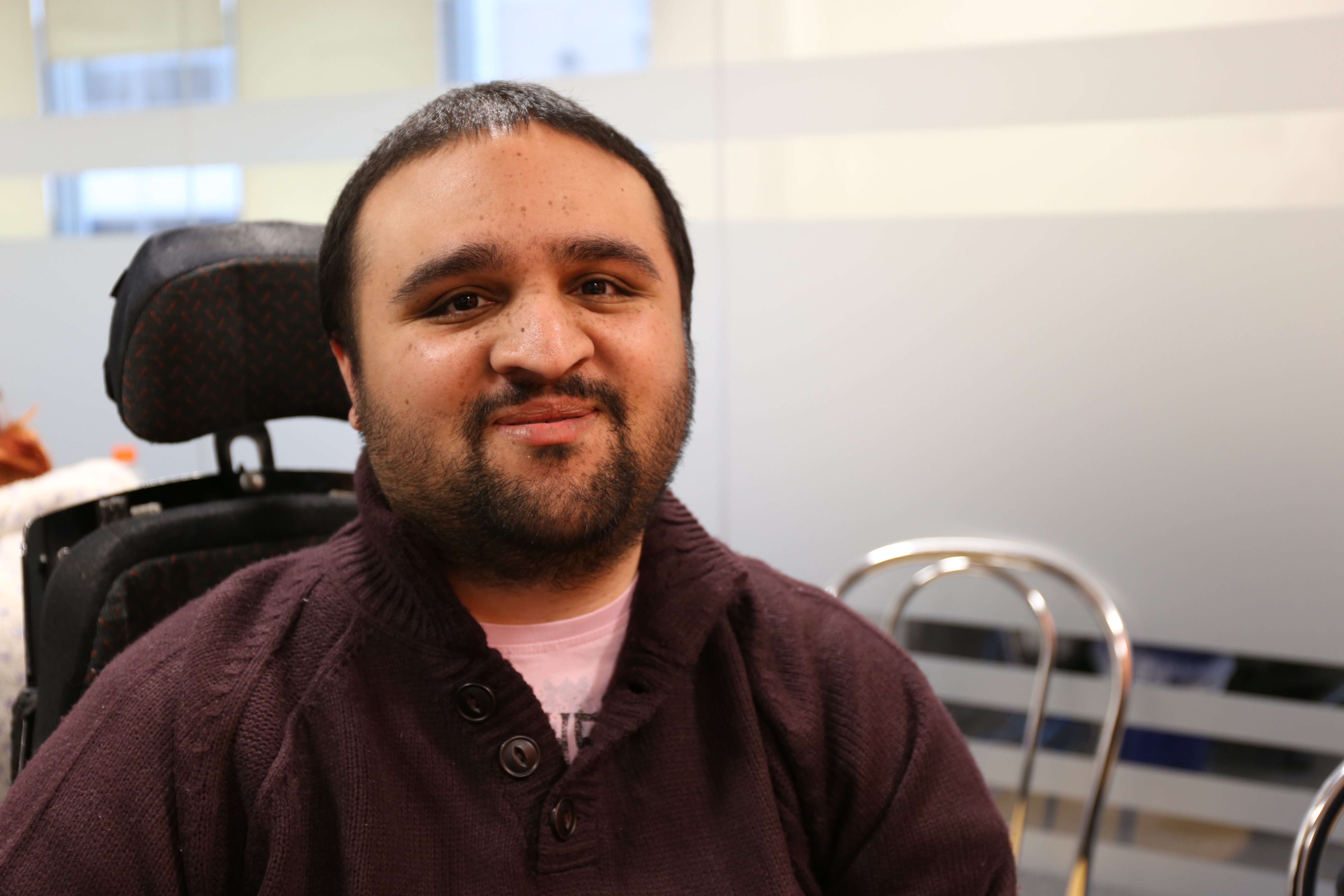A man in a maroon shirt, with dark hair and a beard. He is a wheelchair user.
