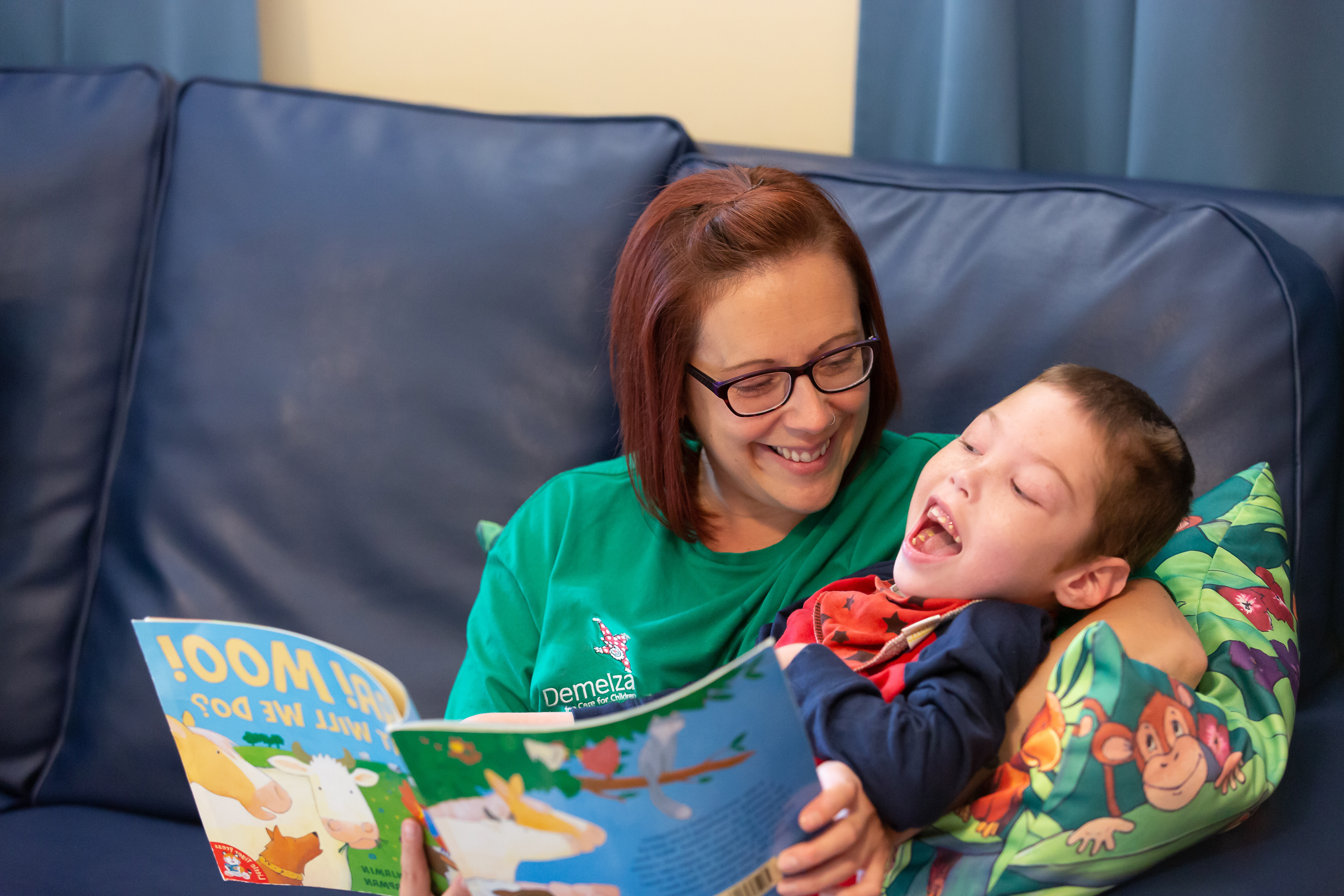 Archie and Health Care Assistant laughing whilst reading a book together