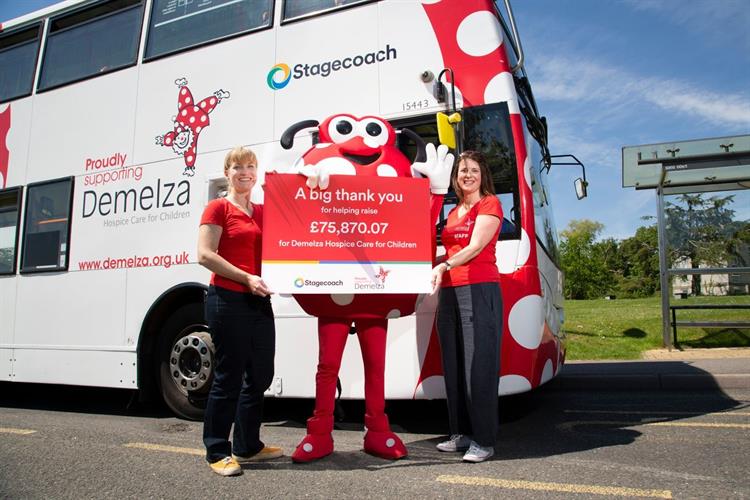 Dotty and two Demelza staff standing in front of a Stagecoach double decker bus, holding a cheque.