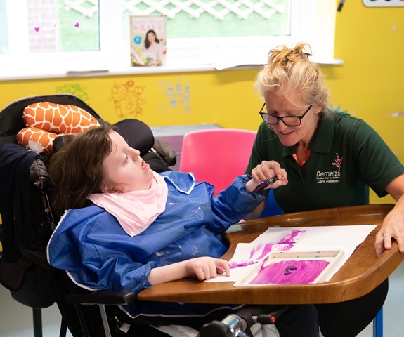 A young girl enjoys a painting activity with a Demelza Health Care Assistant.