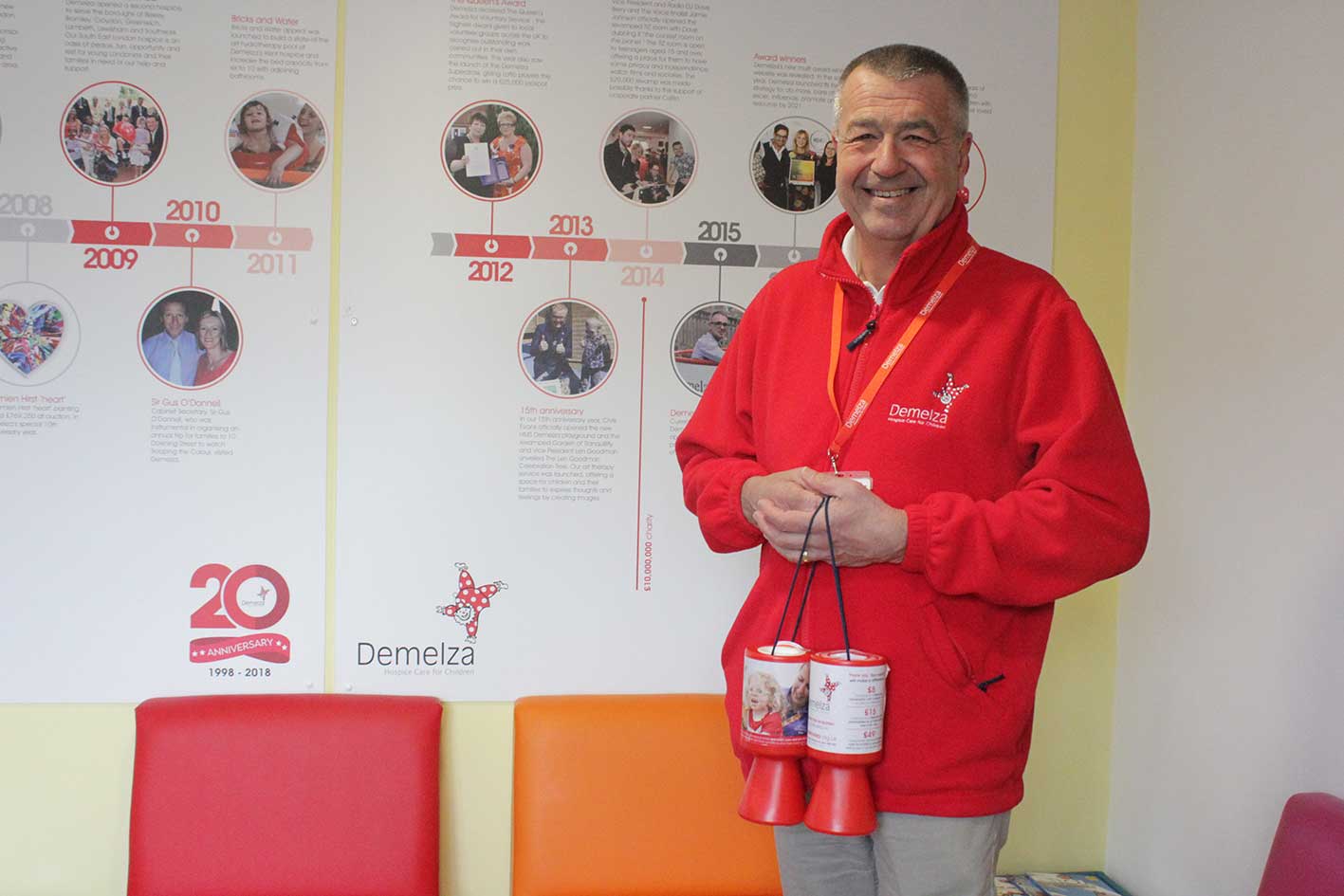A Demelza volunteer wearing a red fleece is holding collection pots.