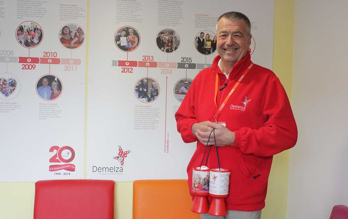 A Demelza volunteer wearing a red fleece is holding collection pots.