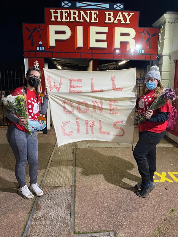 Sky and Abi hold a 'well done' banner at the finish line of their walking marathon, on Brighton Pier.