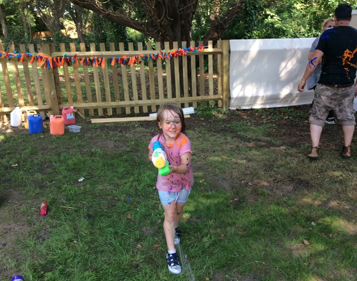 A girl with paint on her face, aims her water pistol at the camera.
