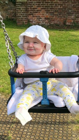 Darcy, sitting in a swing wearing a sun hat.