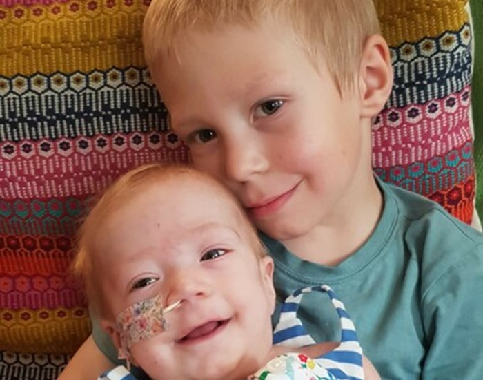 Darcey sits on brother Archie's lap, both are smiling.