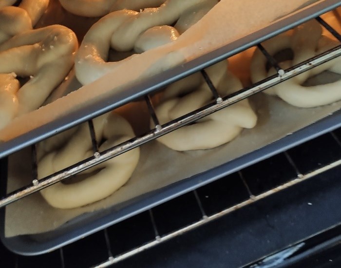 Two trays of large pretzels baking in an oven.