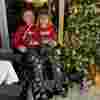 Boy on a wheelchair with his sister on his lap, both wearing christmas jumpers, , smiling whilst next to a christmas tree